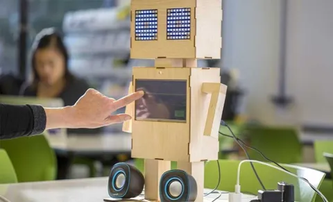 A friendly looking robot clad in wood with a touch screen