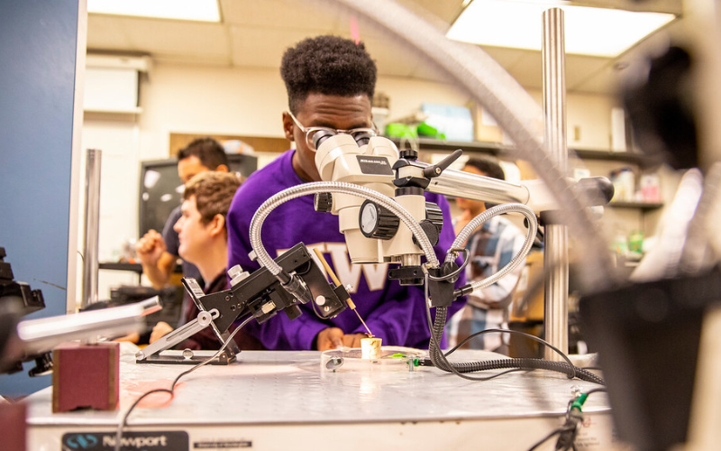 Student wearing W sweater looking into microscope