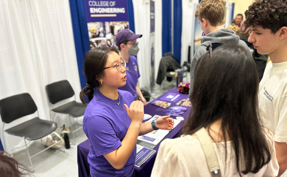 An engineering student speaking to two people at fair