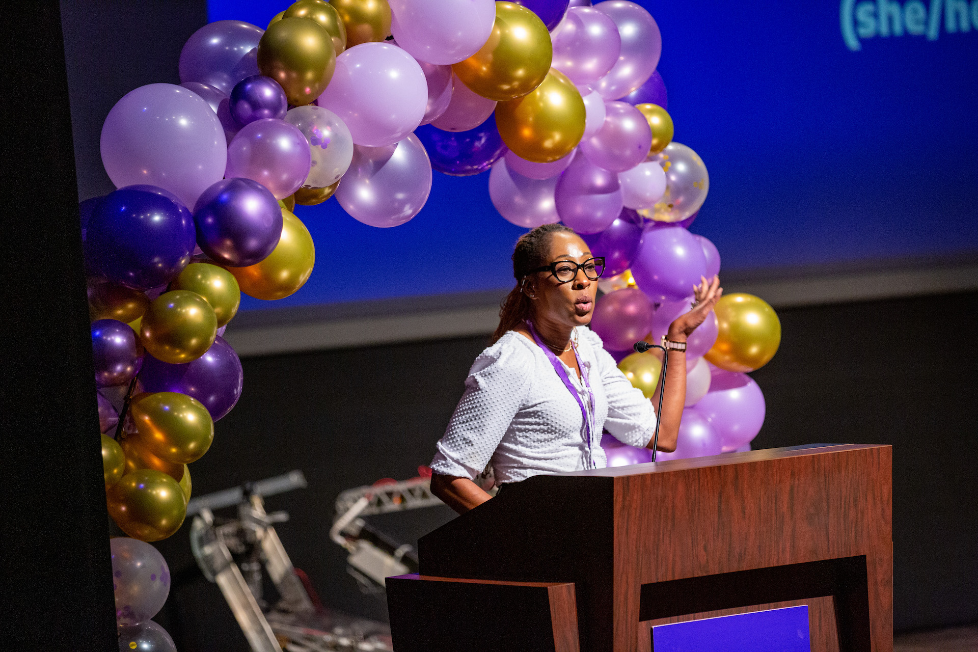 Woman giving a presentation standing at a podium with balloons in the background