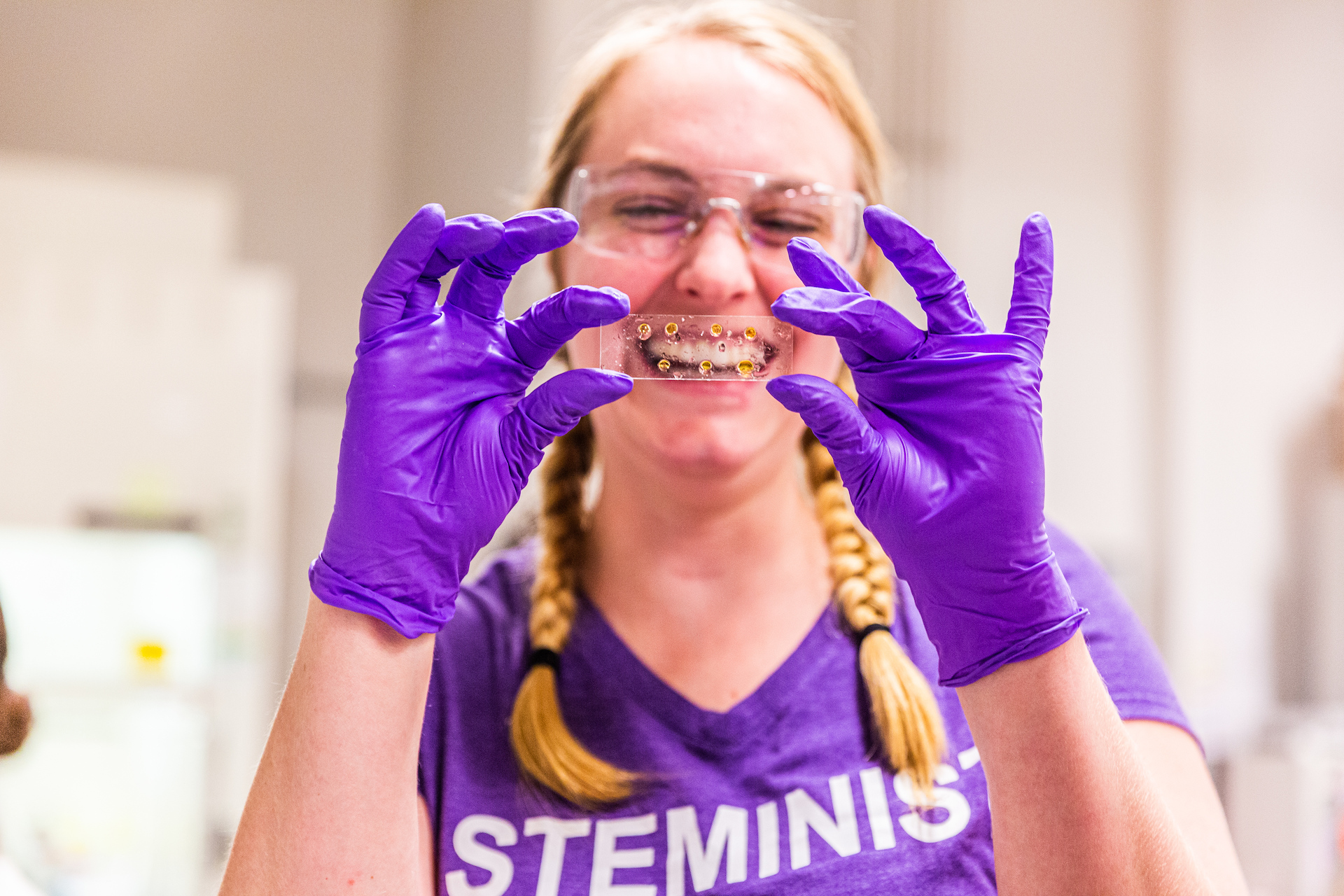 Woman wearing purple gloves and holding a plastic container with a lab sample