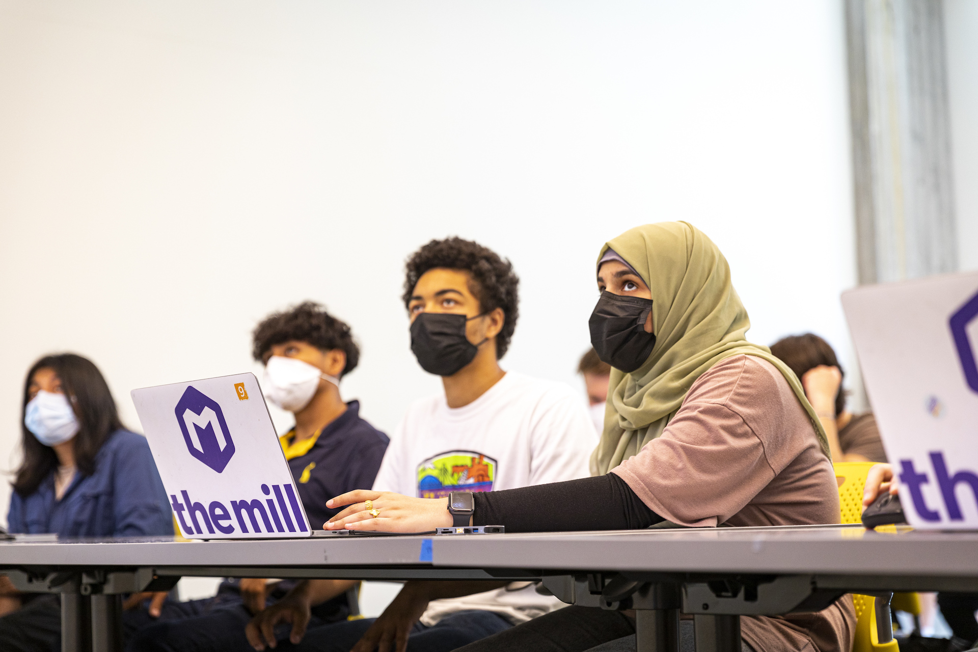 four students during a class sitting in a table with an open laptop