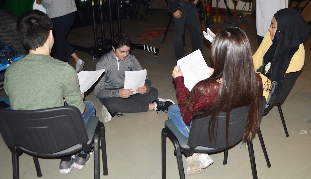 four people sitting in chairs reading scripts