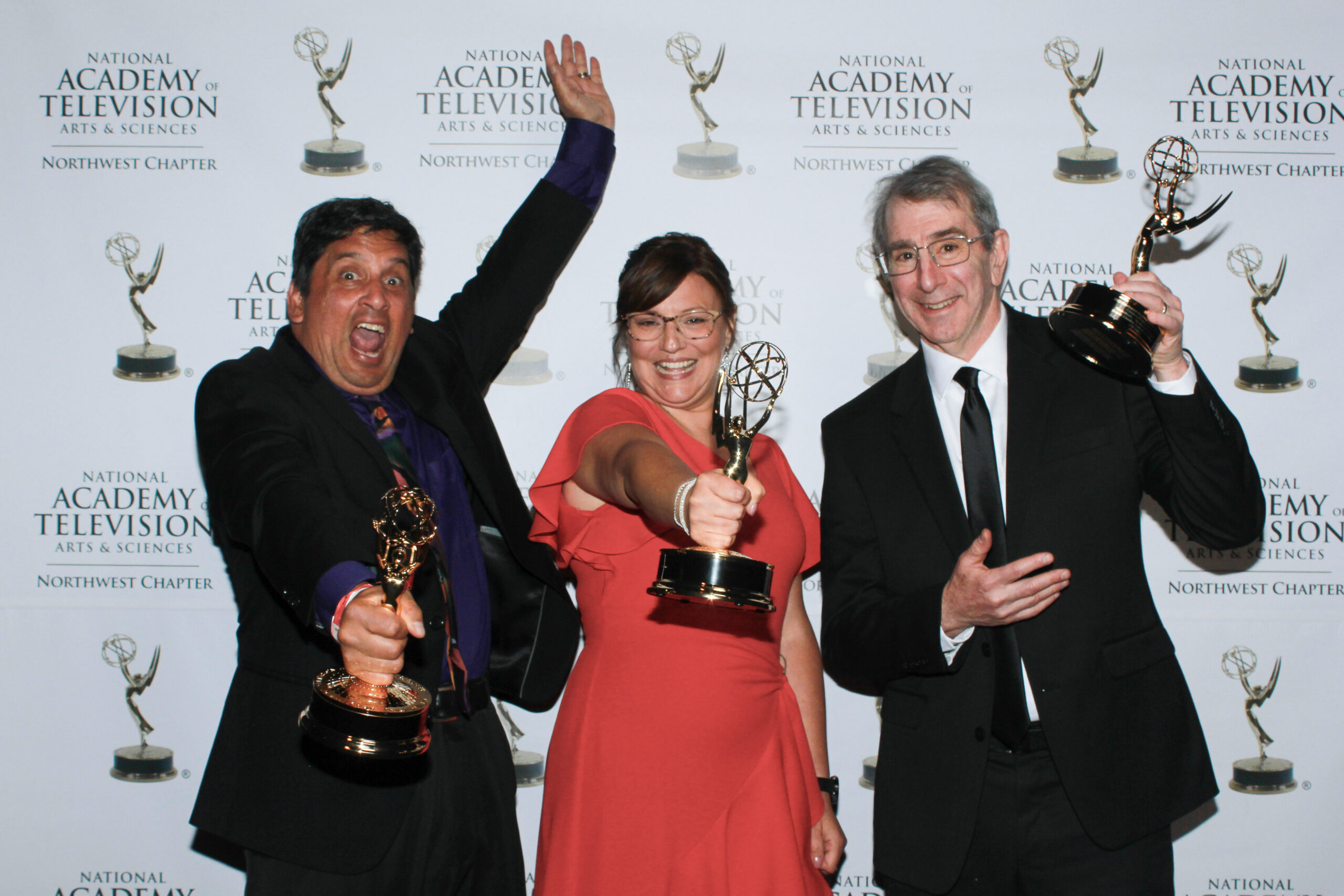 Three people holding Emmy awards and smiling to the camera