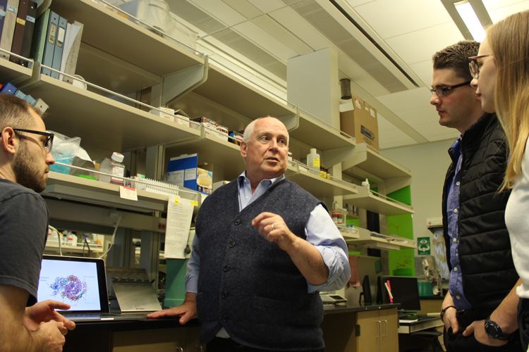 Four people in a laboratory, one man explaining something to the others.