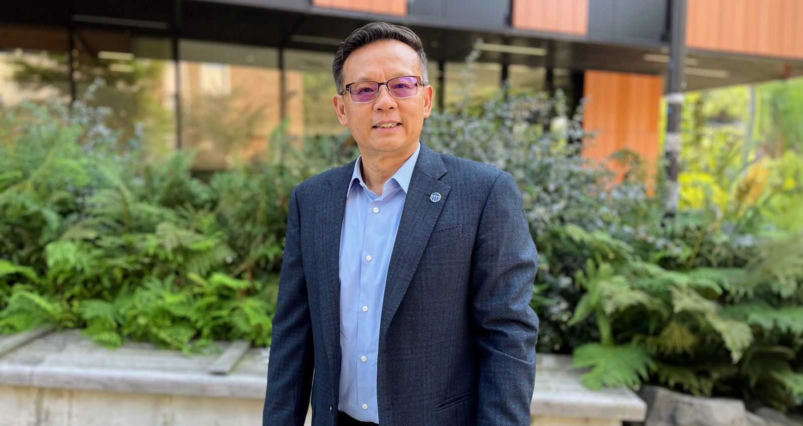 Full profile photo of Juming Tang standing outdoors in front of a research building on campus.