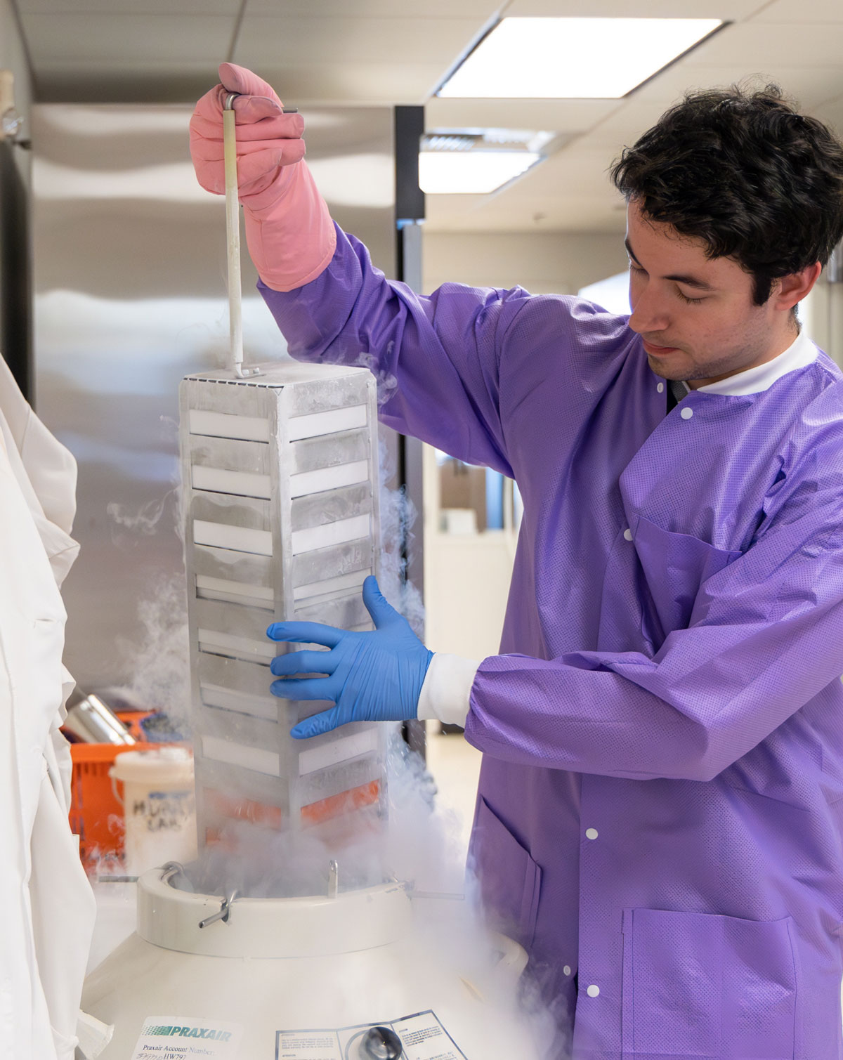 Person in a lab handling a cryogenic storage vessel with vapor.