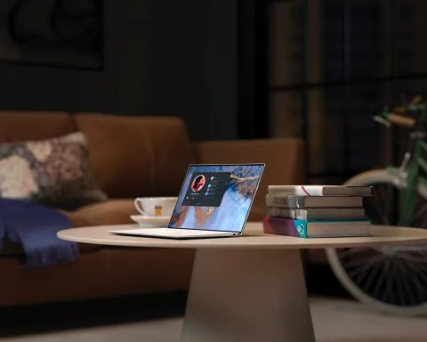 A table in the living room with a cup of tea, a laptop and a stack of books on top. Behind the table is a couch and a bike