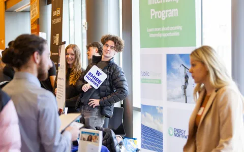 A busy career fair. In the background, a person is holding up a sign that reads "#HireHuskies"