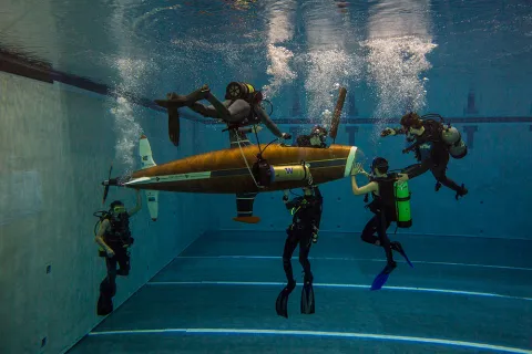 A group of students underwater surrounding a human-powered submarine 