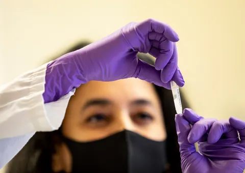 Person wearing gloves and PPE looking at sample in tube