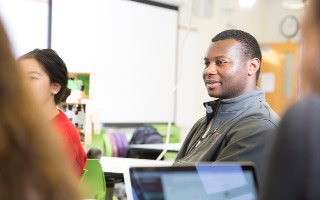 Students sitting around table on laptops listening to lecture