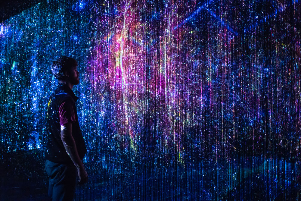 A person in a dark room observing an art display of abstract vertical lights