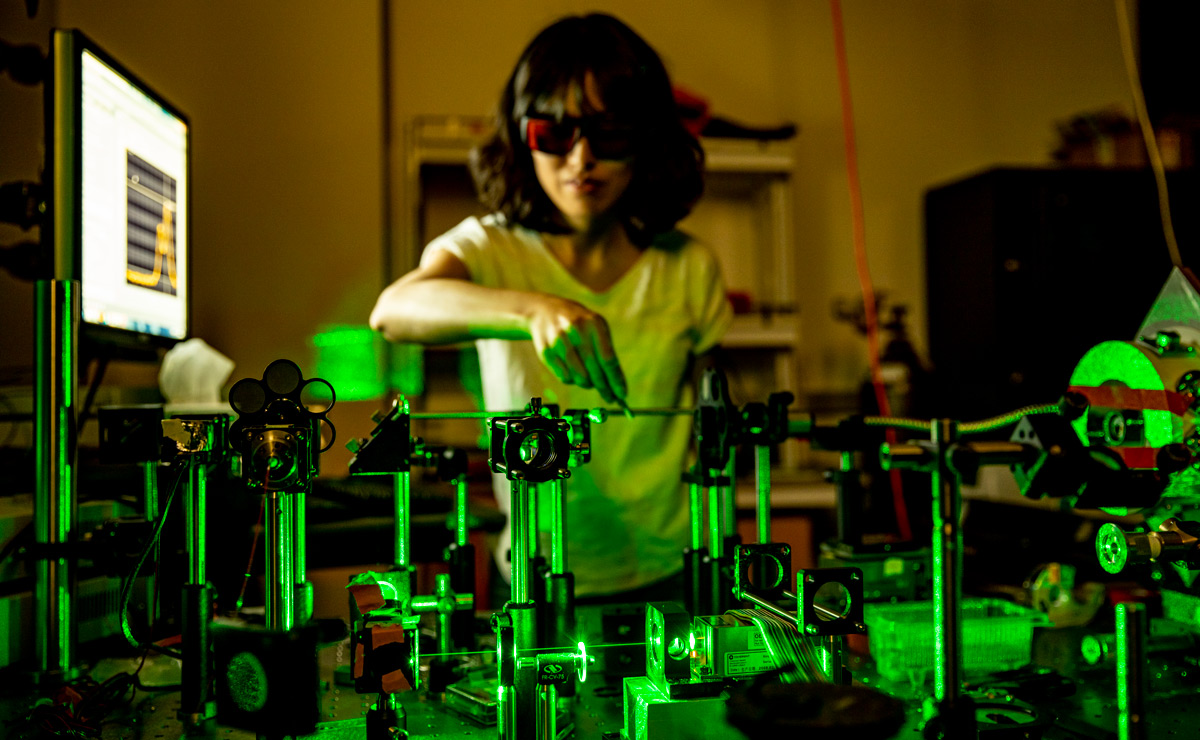 A student wearing safety glasses interacting with a prototype illuminated with green light