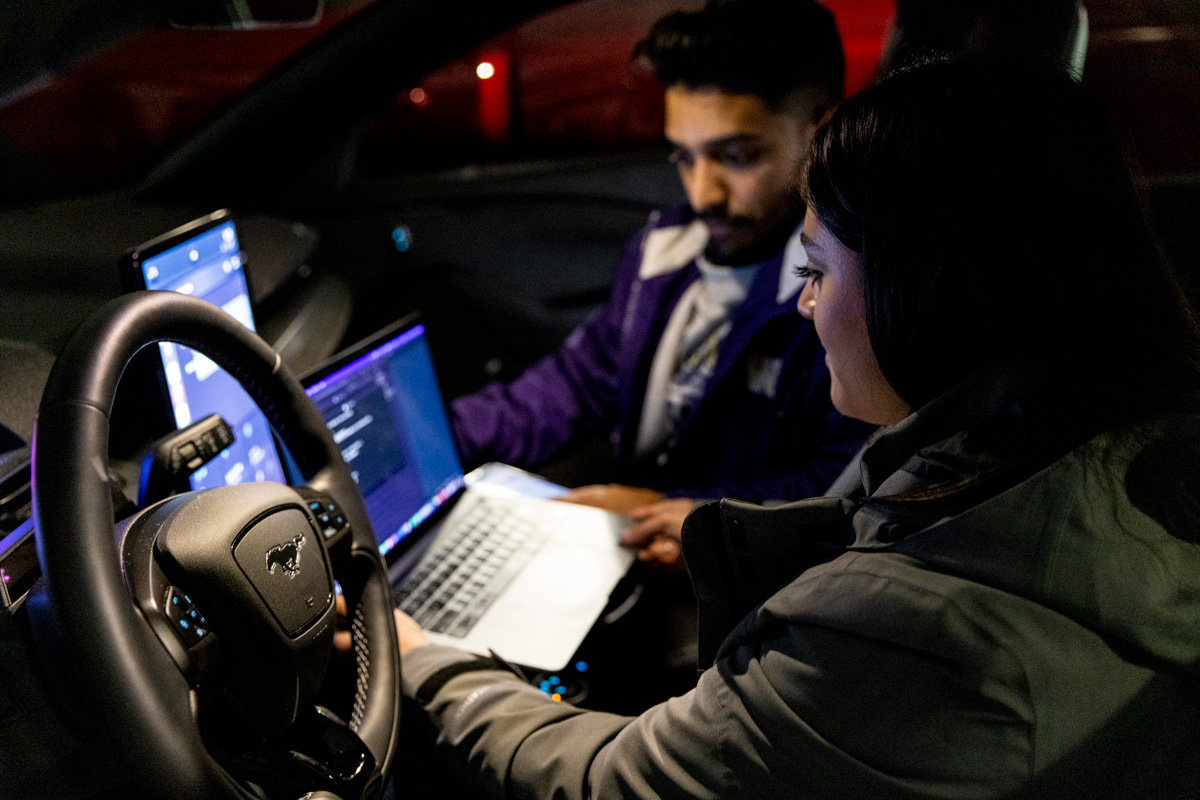 Students working on a laptop inside of an electric vehicle