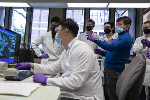 Faculty teaching in lab surrounded by students wearing lab coats