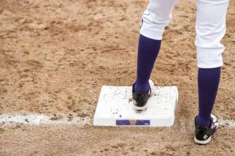 A baseball player's lower legs stepping on a white base.