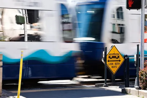 Signs suggest pedestrians look both ways as a Sound Transit train rushes past Othello Station at MLK Way. (Karen Ducey / The Seattle Times)