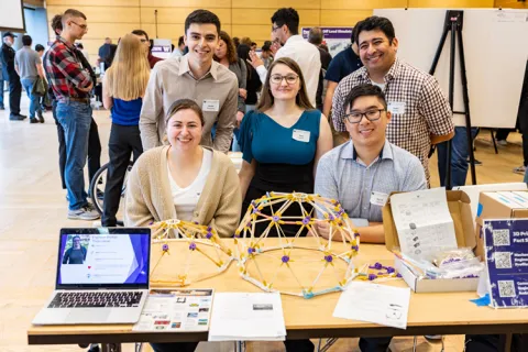 Five students are behind a table that holds domes that are part of a science activity for youth