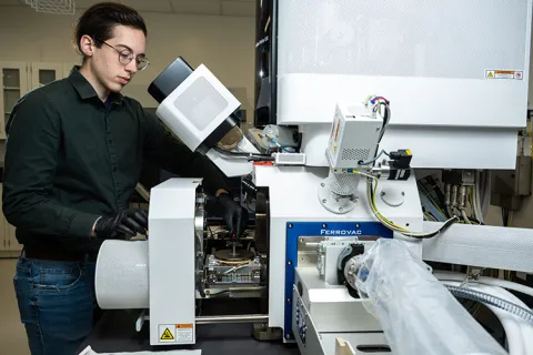 Jack Grimm standing behind ion-beam scanning electron microscope