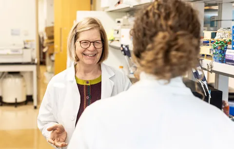 Mary Lidstrom wearing lab coat smiling and speaking to student in lab setting